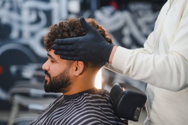 Modern bir berber dükkanında saçları kıvırcık, berber gibi kestirip, eldiven takan bir müşteri.
