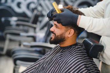 Sakallı bir adam modern bir kuaförde berberden profesyonel saç kesimi ve kuaför hizmeti alıyor, gülümsüyor.