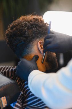 Siyah eldivenli profesyonel berber berber berber dükkanındaki bir adam için temiz bir soluk ve keskin bir sakal çizgisi oluşturuyor.