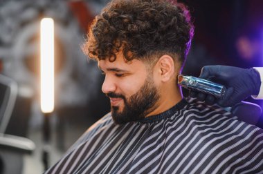 Kıvırcık saçlı ve sakallı rahat bir adam berberden profesyonel saç kesimi ve bakım hizmeti alıyor.