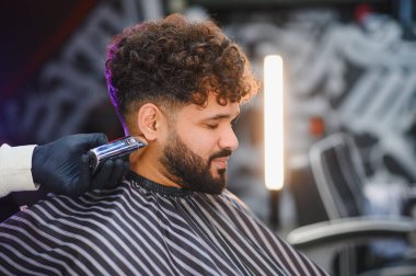 Tıraş makinesiyle sakal ve saç kesen berber stil ve bakım üzerine odaklanıyor.