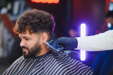 Modern saç kesimi ve sakal kesimi yaptıran bir adam. Moda berberinde kırpıcı kullanıyor.