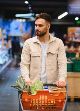 Taze ürün ve sağlıklı yiyeceklerle dolu alışveriş arabalarını iten adam modern bir markette ev yemeği için eşyalar seçiyor.