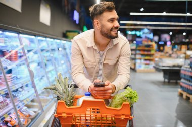 Gülümseyen adam, akıllı telefon uygulamasında ürünler buluyor ve fiyatları karşılaştırıyor.