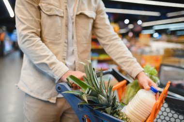 Müşteri taze yiyecek ve temel ihtiyaçlarını seçiyor, modern bir perakende mağazasından alışveriş arabası geçiriyor.