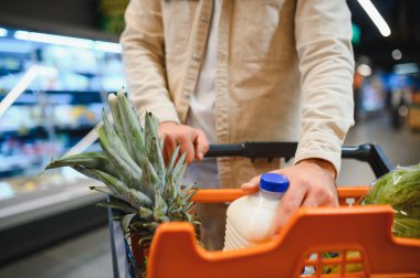 Ananas, süt ve taze ürünlerle alışveriş arabası iten adam. Yerel bir marketten sağlıklı yiyecekler almak.
