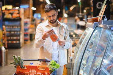 Adam paketlenmiş bir balık ürününü inceliyor, markette alışveriş yaparken yiyecek etiketine dikkat ediyor.