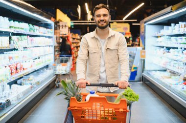 Gülümseyen adam taze yiyecek ve bakkaliye buluyor, iyi stoklanmış bir süpermarkette günlük alışveriş deneyiminin tadını çıkarıyor.