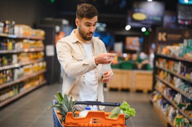 Alışveriş sonrası uzun bir nakit makbuzuna şaşıran bir adam, artan tüketici maliyetleri ve süpermarketteki enflasyonu vurguluyor