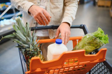 Marketteki ananas, süt ve marul gibi taze ürünlerle dolu bir portakal arabasını iten adam.