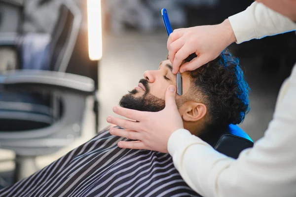 Profesyonel berber, erkek bir müşteriye jiletle yakın traş hizmeti sunuyor, sakal hatlarına odaklanıyor.