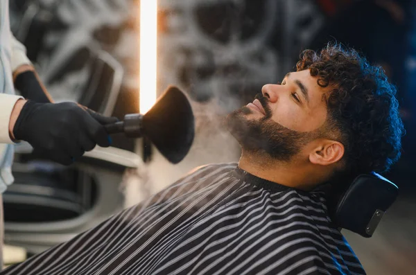 Berber, adamın sakalına ve boynuna pudra sürüp yeni bir tımar seansının tadını çıkarıyor.