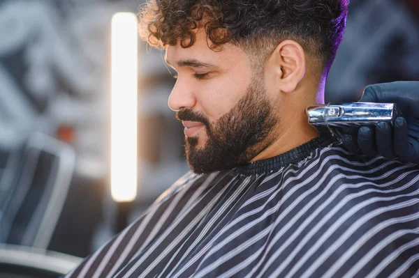 Kıvırcık saçlı ve sakallı bir adam modern kuaförde berberden kesin boyun kesimi, odaklanmış bakım ve profesyonel bakım alıyor.