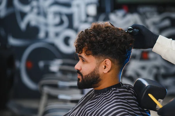 Saç stili bir adamın kıvırcık saçlarını makasla kesmesi, soluk bir saç kesimi yaratması ve sakalını koruması.