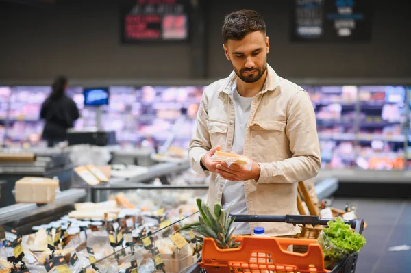 Elinde paketlenmiş peynir olan bir adam süpermarkette alışveriş arabasının yanında dururken satın alma kararı veriyor.