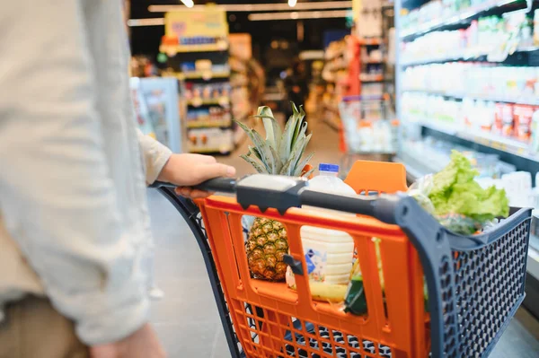 Müşteri taze ürünler ve sebzeler seçiyor, turuncu alışveriş arabasını bulanık bir süpermarket koridorunda itiyor.