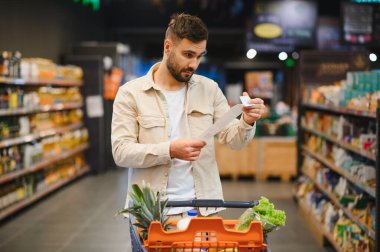 Markette alışveriş yapan kişi, artan gıda maliyetleri ve enflasyon kaygıları nedeniyle ev bütçesini yönetmek için fatura ve karşılaştırma yapıyor