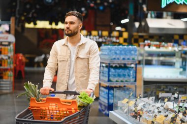 Genç adam markette içi taze ürünlerle dolu alışveriş arabalarını itiyor. Tüketici sağlıklı seçimler yapıyor