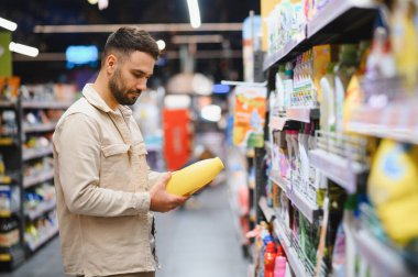 Perakende mağazasında temizlik malzemeleri alırken bir ürün etiketini inceleyen adam tüketici seçimi yapıyor.