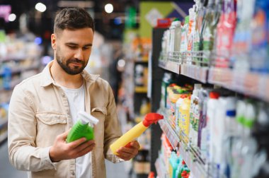 Süpermarketin rafındaki farklı temizlik ürünleri arasından alışveriş yapan bir adam satın alma seçimi yapıyor.