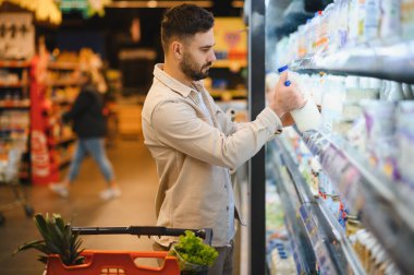 Elinde bir şişe süt tutan bir adam, marketin dondurulmuş süt reyonundan alışveriş yapıyor, sağlıklı bir ürün seçimi yapıyor.