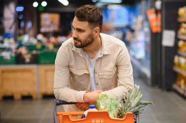Taze ürün ve sütle dolu bir alışveriş arabasını iten düşünceli bir adam.