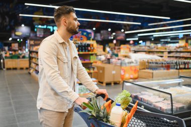 Canlı bir süpermarket koridorunda alışveriş arabası taşıyan bir adam sağlıklı yaşam için yiyecek seçiyor.
