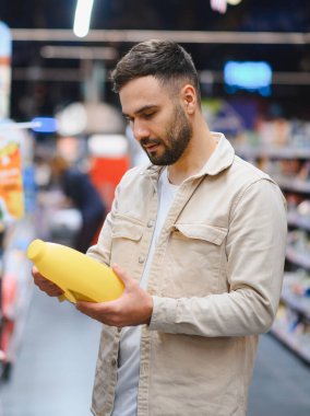 Marketteki adam ürünleri karşılaştırıyor ve satın alma kararı veriyor, sarı bir şişeye odaklanıyor.