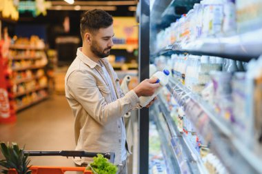 Mandıra ürünleri almak için müşteri alışverişi, süpermarket koridorundaki süt şişesinin etiketini kontrol etmek,