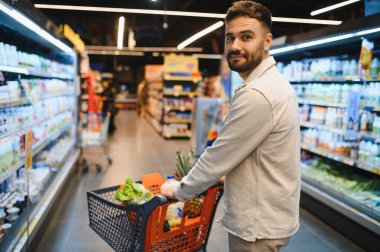 Bakkal koridorunda içi taze sebze dolu alışveriş arabalarını iten adam geriye bakıyor.