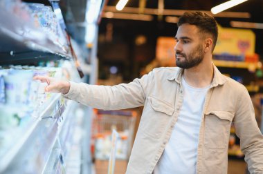Modern bir marketin süt ürünleri bölümünde dondurulmuş bir rafa uzanan bir adam tüketici seçimi yapıyor.