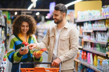 Bakkal koridorunda sprey temizleme ürünlerini karşılaştıran genç bir çift aile alışverişi sırasında gülümsüyor.