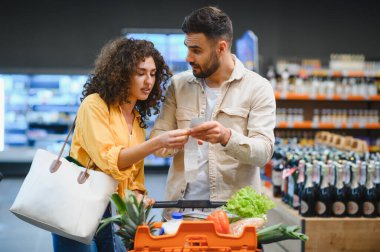 Market alışverişi makbuzuna bakan çift, süpermarket ziyareti sırasında aile bütçesini hesaplıyor, yüksek yaşam maliyetinden endişe ediyor.