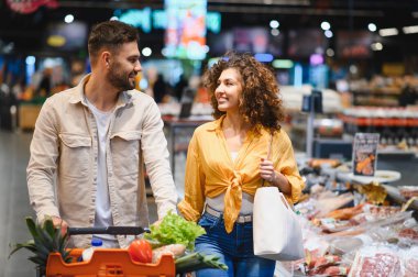 Taze ürünlerle dolu alışveriş arabasını iten gülümseyen genç çift, bakkalda birlikte vakit geçiriyorlar.