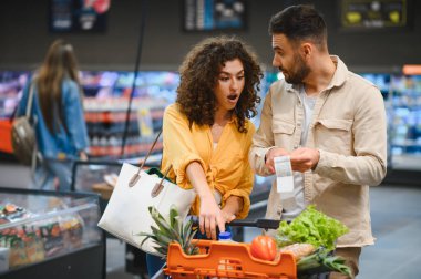 Uzun bir market fişine bakan genç çift, süpermarkette alışveriş yaparken yüksek maliyetli ürünlere şaşırdı.