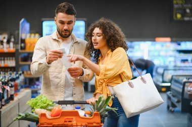 Markette market faturalarını karşılaştıran, ev bütçesini yöneten ve harcamaları takip eden genç bir çift.