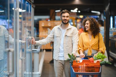 Genç çift taze ürünleri ve dondurulmuş yiyecekleri seçiyor, modern bir marketten gerekli malzemeleri alırken zamanlarının tadını çıkarıyorlar.