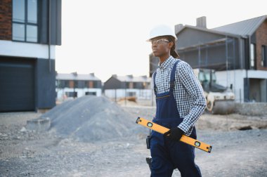 Siyah adam yeni bir inşaat projesinde inşaat aletini taşırken kasket ve güvenlik gözlüğü takıyor.