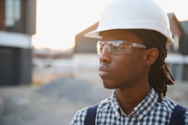 Rastalı erkek müteahhit, başlık takıyor ve güvenlik gözlüğü takıyor. İnşaat alanının inşaatını dört gözle bekliyor.