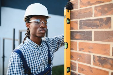 Afrikalı Amerikalı inşaatçı, inşaat kalitesi ve hassasiyetini güvence altına almak için yeni bir tuğla duvarda düz bir alet kullanıyor.