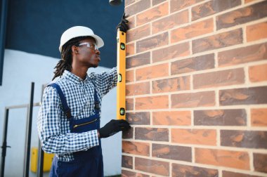 Profesyonel inşaat işçisi yeni bir tuğla duvarda ruh seviyesini kullanarak inşaat çalışmalarının doğruluğunu ve kalitesini sağlıyor.