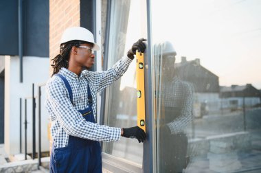 Afrikalı Amerikalı inşaat işçisi pencere kuruyor, hizalama ve yeni bir bina projesinde seviye kontrolü yapıyor