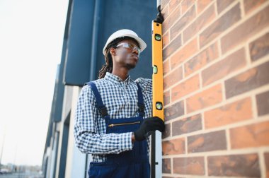 Siyah şapka takan ve güvenlik gözlüğü takan Afrikalı Amerikalı işçiler tuğla duvarın dikeyliğini ölçüyor.