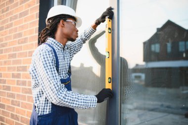 Afro-Amerikan işçiler ticari bina inşaatı sırasında bir ruh seviyesi aracı ile pencere çerçeve seviyesini kontrol ediyorlar