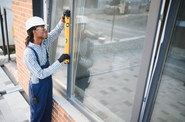 Profesyonel inşaat işçisi modern tuğla bir binaya yeni bir pencere çerçevesi yerleştiriyor.