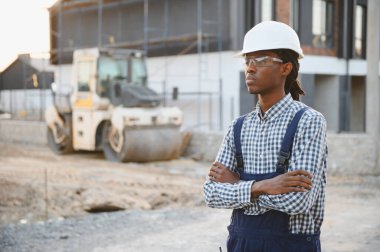 Siyah şapkalı ve güvenlik gözlüklü Afro-Amerikan işçiler, açık hava inşaatında çapraz kollarla duruyorlar.