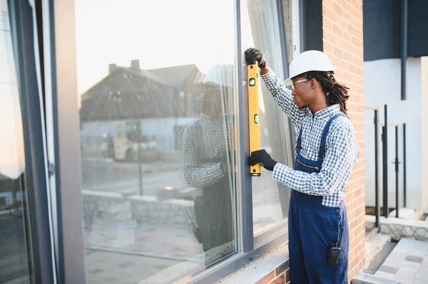 Genç bir siyahi inşaat işçisi modern bir inşaat alanının pencere kurulumu için ruh seviyesinde bir araç kullanıyor.
