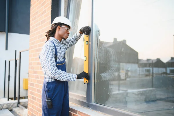 Tecrübeli Afro-Amerikan inşaat işçisi. Yeni bir konut inşaatı sırasında pencere çerçevesini kontrol ediyor.