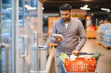 Markette alışveriş arabasıyla alışveriş yapan bir adam, bir perakende mağazasında satın alma kararı alır.