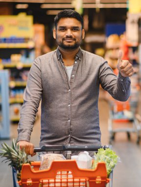 Gülümseyen bir adam marketteki perakende satış deneyimini onaylayan bir alışveriş arabasını itiyor.